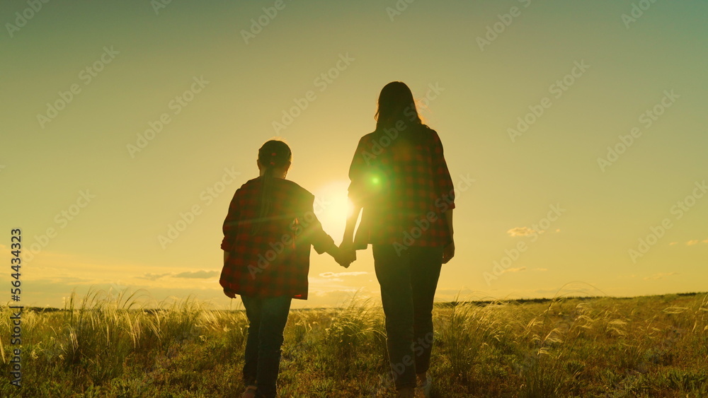Happy family, mom, daughter hold hands walk together in acre in autumn. Active lifestyle. Mother, daughter, child go hand in hand at sunset in field. Parent, girl, child, happy childhood, Motherhood.