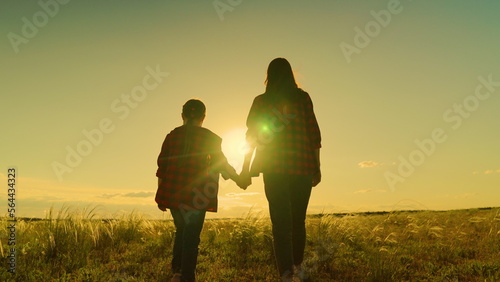 Happy family, mom, daughter hold hands walk together in acre in autumn. Active lifestyle. Mother, daughter, child go hand in hand at sunset in field. Parent, girl, child, happy childhood, Motherhood.