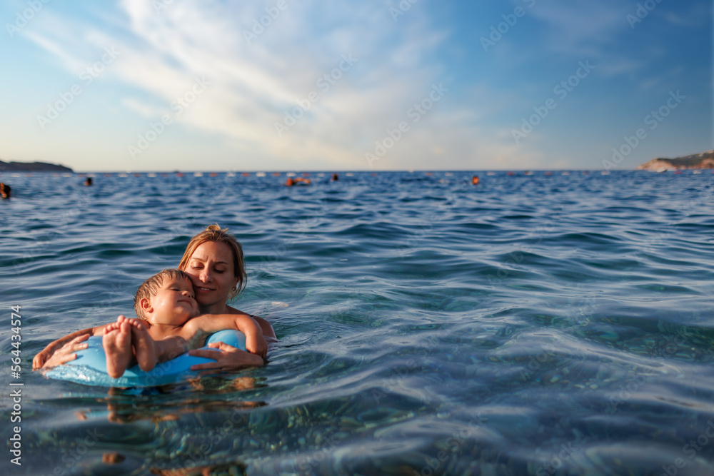 Caring mother rides her son on an inflatable ring in the sea