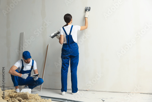 Professional workers plastering wall with putty knives indoors photo