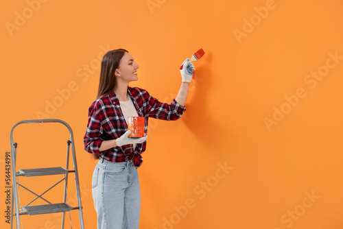Designer painting orange wall with brush, space for text
