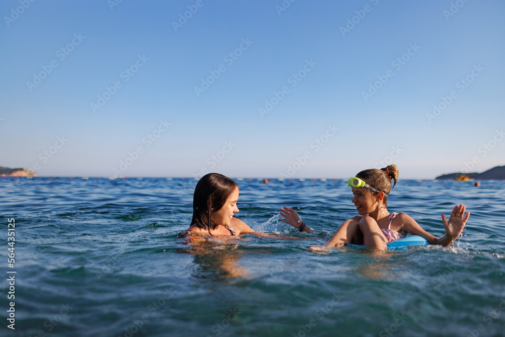 Two sisters in bathing suits play with an inflatable ring in the sea