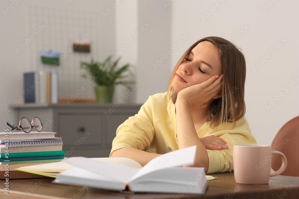 Young tired woman studying at wooden table in room Young tired woman studying at wooden table in room