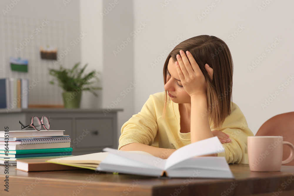 Young tired woman studying at wooden table in room Young tired woman studying at wooden table in room