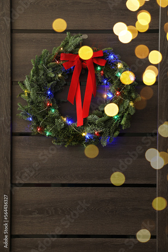 Beautiful Christmas wreath with red bow and festive lights hanging on door