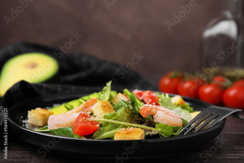 Delicious salad with croutons, avocado and shrimp served on wooden table, closeup