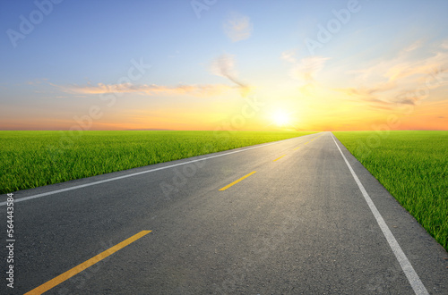 Strait tarmac road in slope grass field with sunset background.
