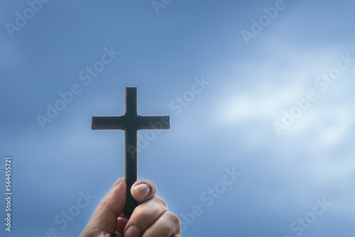 Hand holding a wooden cross crucifix with blue cloudy sky at the background. Concept for Christian faith and Good Friday.