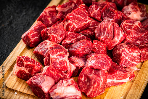 Raw pieces of beef on a wooden cutting board.