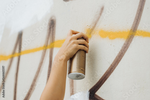 the white hand of an artist holding a spray paint can while painting a mural in broad daylight (ID: 564460597)