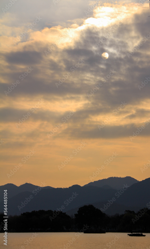 A silhouette boat sailing on the calm sea at sunset in the background of mountains and moon. Gold and yellow color. For travel, background and blog etc. concepts. West Lake. 