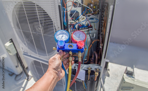 Air conditioning, HVAC service technician using gauges to check refrigerant and add refrigerant.