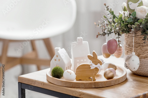 A beautiful postcard. The concept of the Bright Easter holiday. Flowers, rabbits, Easter eggs and Scandinavian white houses on a wooden table in a cozy living room.