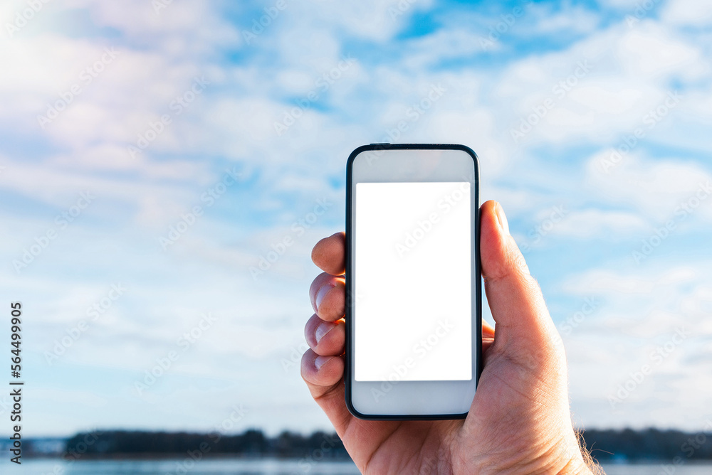 Mockup image of hand holding white mobile phone with blank white screen in blue sky white cloud background.Copy space.