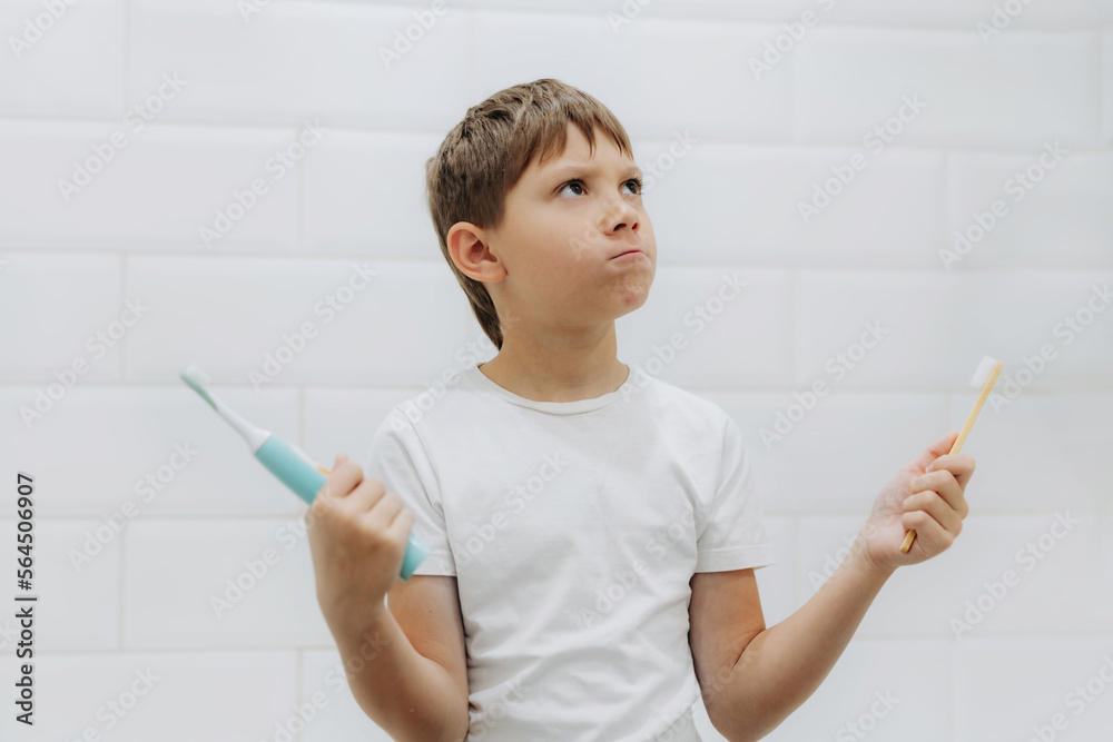 cute 8 years old boy holding bamboo and electric tooth brush making choice cute 8 years old boy holding bamboo and electric tooth brush making choice