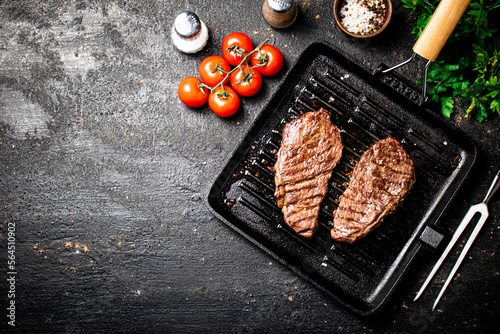 Grilled steak in a frying pan with tomatoes and spices.