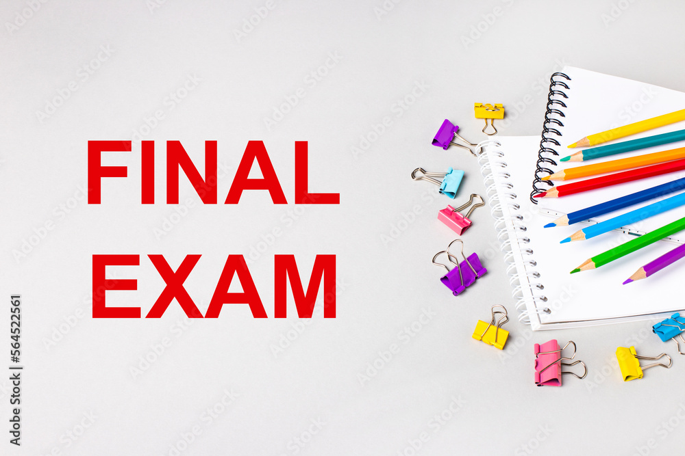 Notebooks, colored pencils and paper clips on a light gray table. The inscription FINAL EXAM. Banner