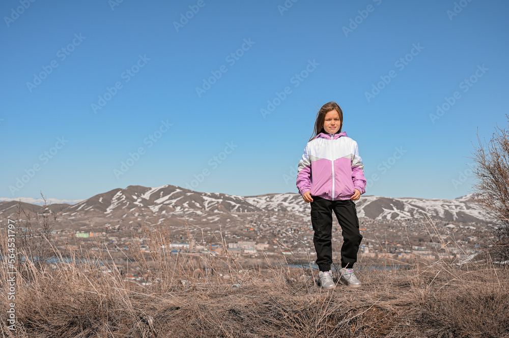 A teenage girl walks through the mountains. Happy young girl in a jacket in the wind. A walk in the fresh air.