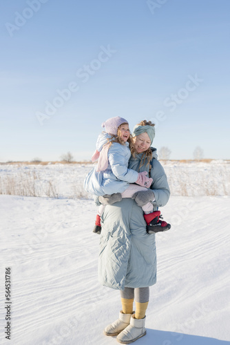 A pregnant young woman holds her daughter in her arms, standing in nature in winter