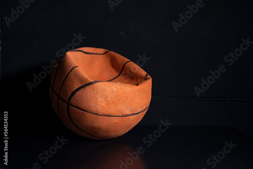 Old deflated basketball black dark background, worn out damaged ball photo