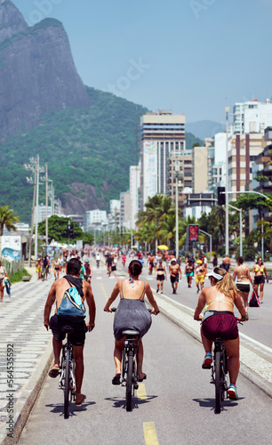 back view of people riding bikes on the bike path on Ipanema beach and people doing sports in the background