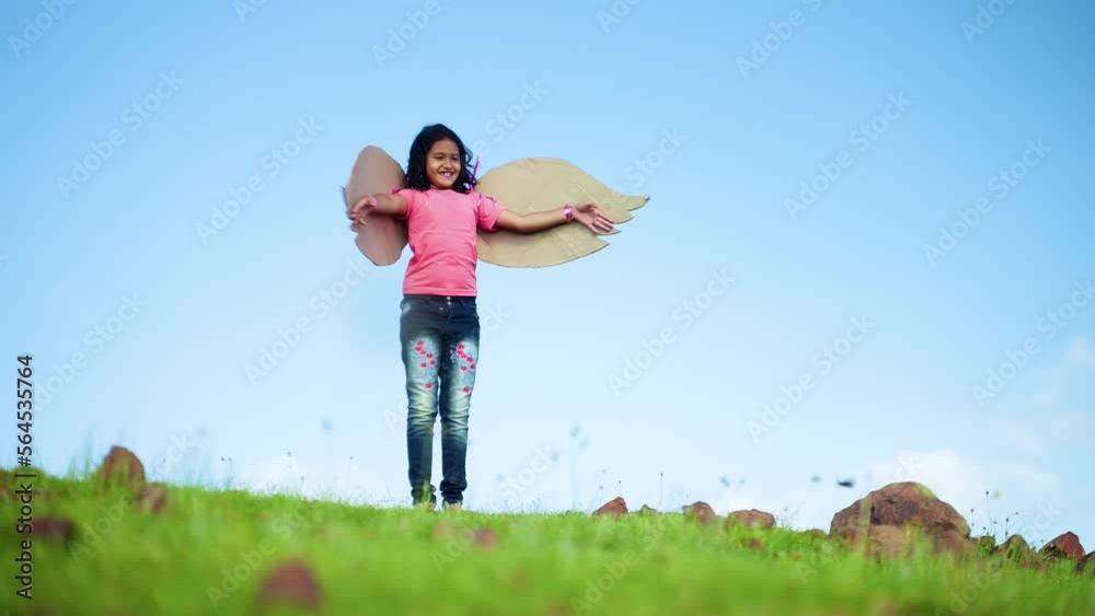 happy excited girl child with wings dancing like a bird on top hill in green meadow against blue sky - concept of freedom, aspirations and imagination happy excited girl child with wings dancing like a bird on top hill in green meadow against blue sky - concept of freedom, aspirations and imagination
