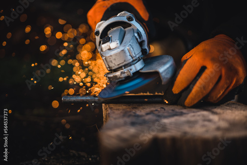 The hands of the master saw the metal with a grinder. Metal works in the workshop close up. Metal processing with angle grinder. Sparks in metalworking. © Peter