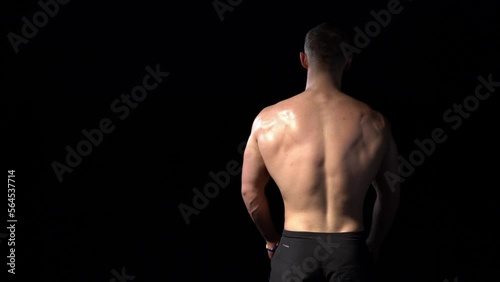 Back view of a muscular shirtless man playing with muscles