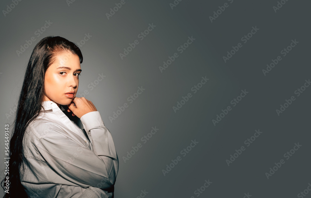 studio portrait o young woman with long black hair touching her chin looking at camera against grey background with copy space studio portrait o young woman with long black hair touching her chin looking at camera against grey background with copy space