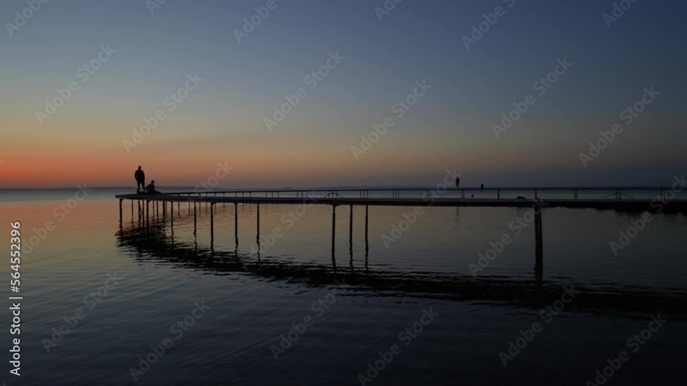 People Sitting And Standing On A Seaside Jetty At Sunset People Sitting And Standing On A Seaside Jetty At Sunset