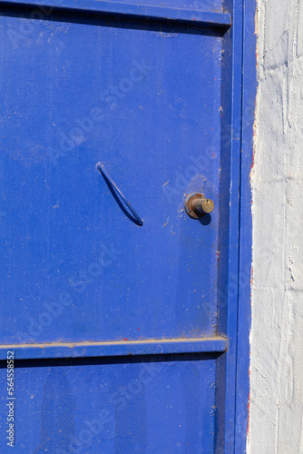 Old, blue, metal door in the white wall.