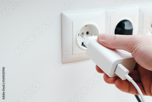 Fotografie Man hands plugging the charger into an outlet in the wall, close-up