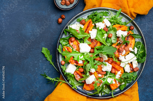Fresh salad with grilled peach and feta cheese, hazelnuts and arugula on blue table background, top view, copy space
