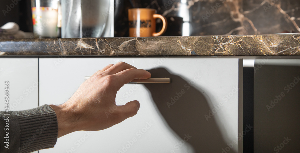 Male hand opening kitchen cupboard door.