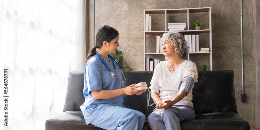 Happy senior woman having her blood pressure measured in a nursing home by her caregiver. Happy nurse measuring blood pressure of a senior woman in living room