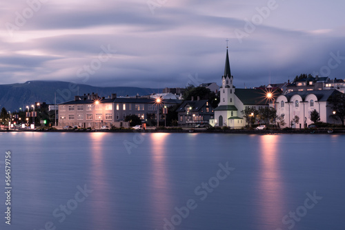 An evening long exposure landscape of Reykjavik city centre with Fr  kirkjan church over the Tj  rnin lake with blurry clouds on the sky and light reflections on the water