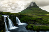 Long exposure landscape of icelandic Kirkjufell mountain covered with green grass with waterfall on the foreground and cloudy sky