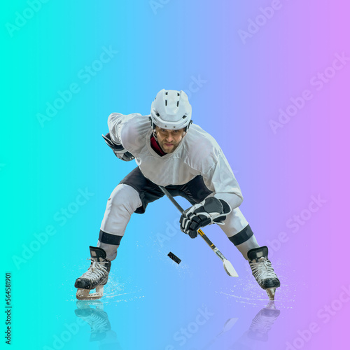 Professional ice hockey player hitting puck for winning goal in action on gradient multicolored neon background. Concept of sport competition. © Andrii IURLOV