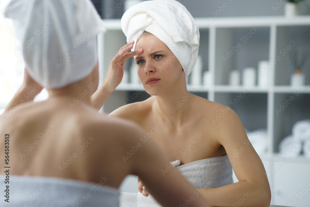 Young woman sits in the bathroom in front of the makeup mirror and does cosmetic procedures. Beautiful girl in white towel. Skin care, health, rejuvenation and spa treatment concept. Young woman sits in the bathroom in front of the makeup mirror and does cosmetic procedures. Beautiful girl in white towel. Skin care, health, rejuvenation and spa treatment concept.