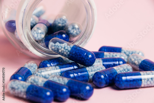 Vitamins in tablet form. Blue pills and transparent jar close-up on pink paper background