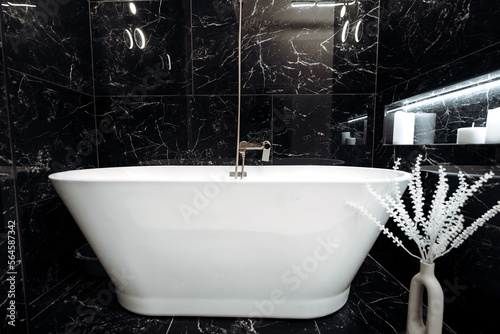 Close up details of freestanding bathtub in modern bathroom with black marble tones