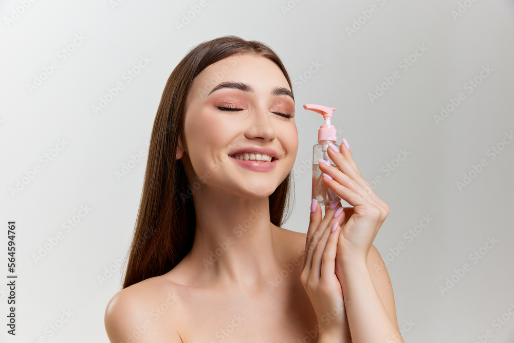 Beautiful young girl with perfect well-lept skin and nude makeup posing with cosmetics over grey studio background. Organic care. Concept of natural beauty, skin care, cosmetology, cosmetics, health Beautiful young girl with perfect well-lept skin and nude makeup posing with cosmetics over grey studio background. Organic care. Concept of natural beauty, skin care, cosmetology, cosmetics, health