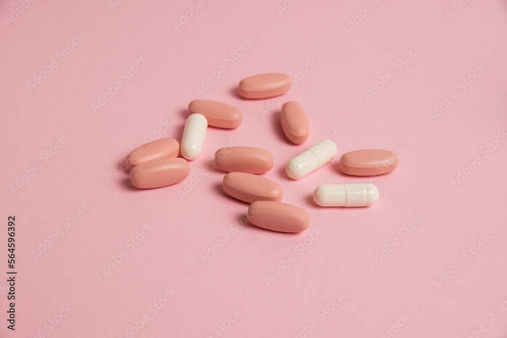 Pink pills and white medical capsules on pink paper background with copy space. The concept of taking vitamins in tablet form Pink pills and white medical capsules on pink paper background with copy space. The concept of taking vitamins in tablet form