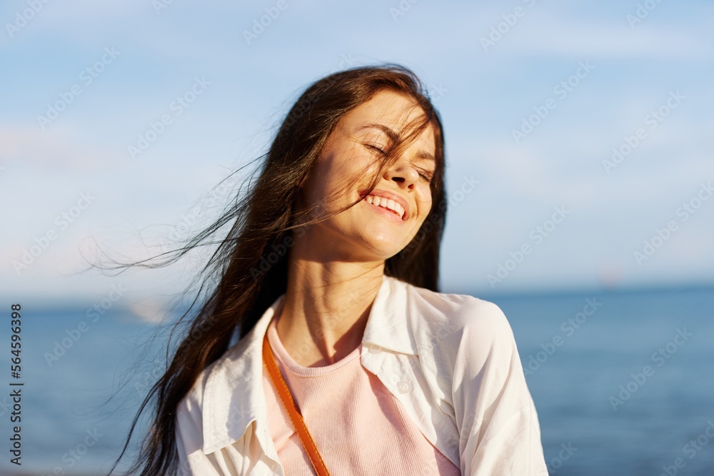 A girl with her eyes closed in the sun against an ocean backdrop smiling with teeth, flying hair, tanned skin, relaxing, traveling to the ocean. A girl with her eyes closed in the sun against an ocean backdrop smiling with teeth, flying hair, tanned skin, relaxing, traveling to the ocean.
