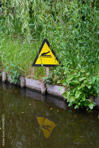 A yellow sign near the pond tells that there is a crocodile under the water. Beware of the dangerous crocodiles in Europe