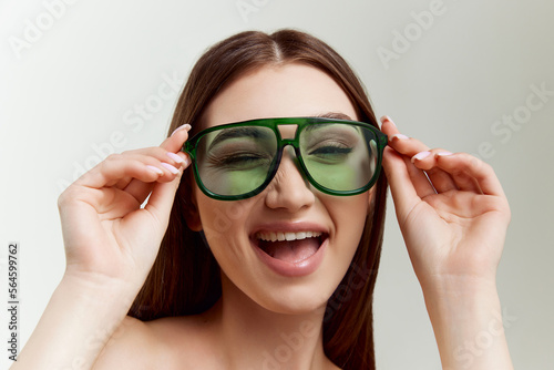 Young beautiful girl with well-kept skin  in green sunglasses posing over grey studio background. Showing positive vibe. Concept of natural beauty  youth  fashion  cosmetology  wellness  makeup.