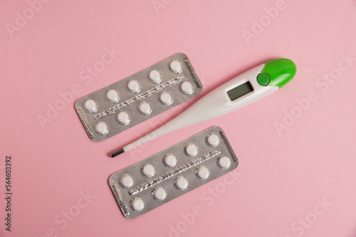 Flat lay, blisters with pills and electronic thermometer on pink paper background with space for text