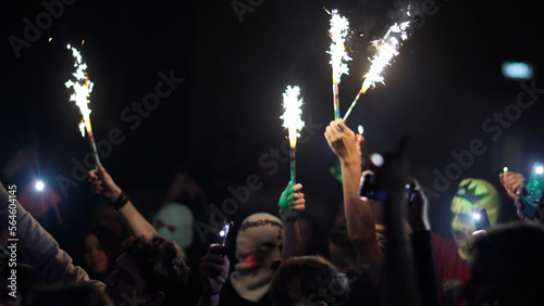 Fans Raise Hands with glowing sparklers in Front of Bright Colorful Strobing Lights on Stage.