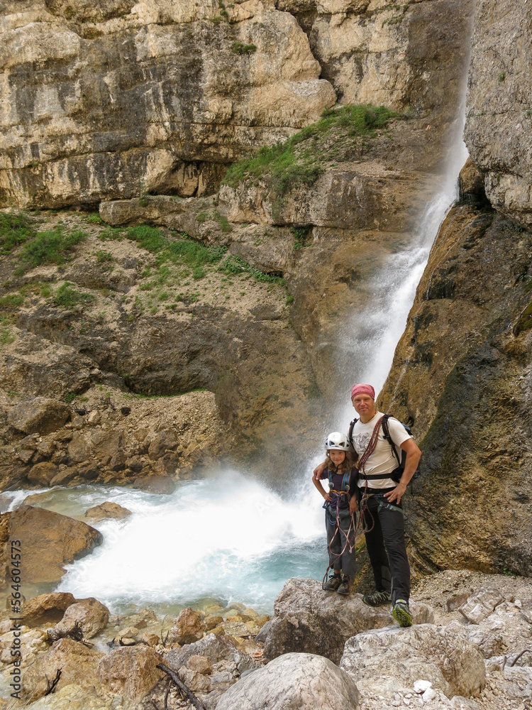 father and daughter trekking near waterfall in Italy Dolomites