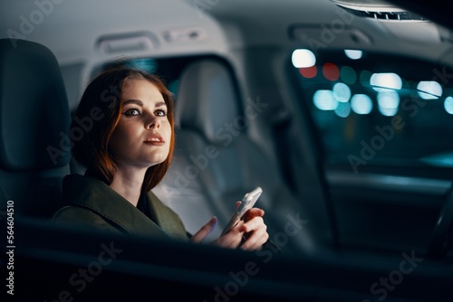 a close horizontal portrait of a stylish, luxurious woman in a leather coat sitting in a black car at night on the passenger seat, thoughtfully looking out the open window of the car © SHOTPRIME STUDIO
